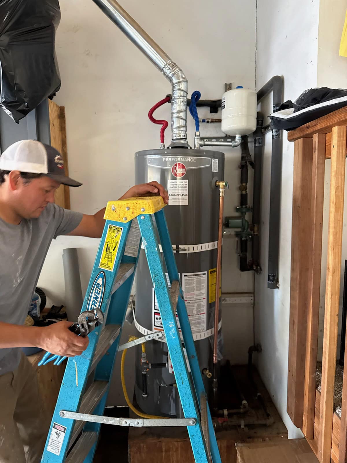 Technician using a blue ladder to service a silver water heater in El Dorado County, CA for Murray Plumbing