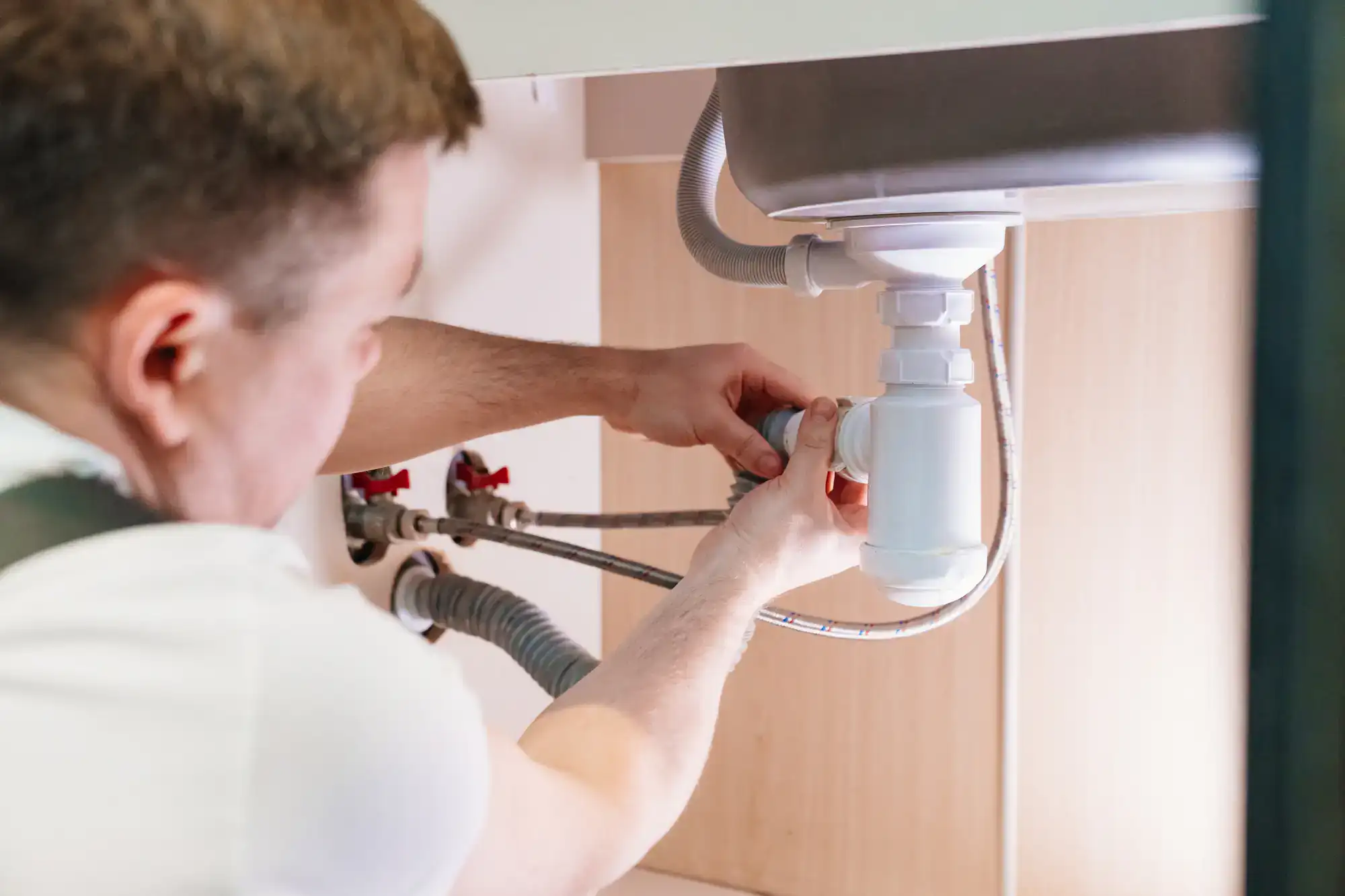 Plumber repairing a pipe under the kitchen sink in El Dorado County, CA, offering expert plumbing services with precision and care.